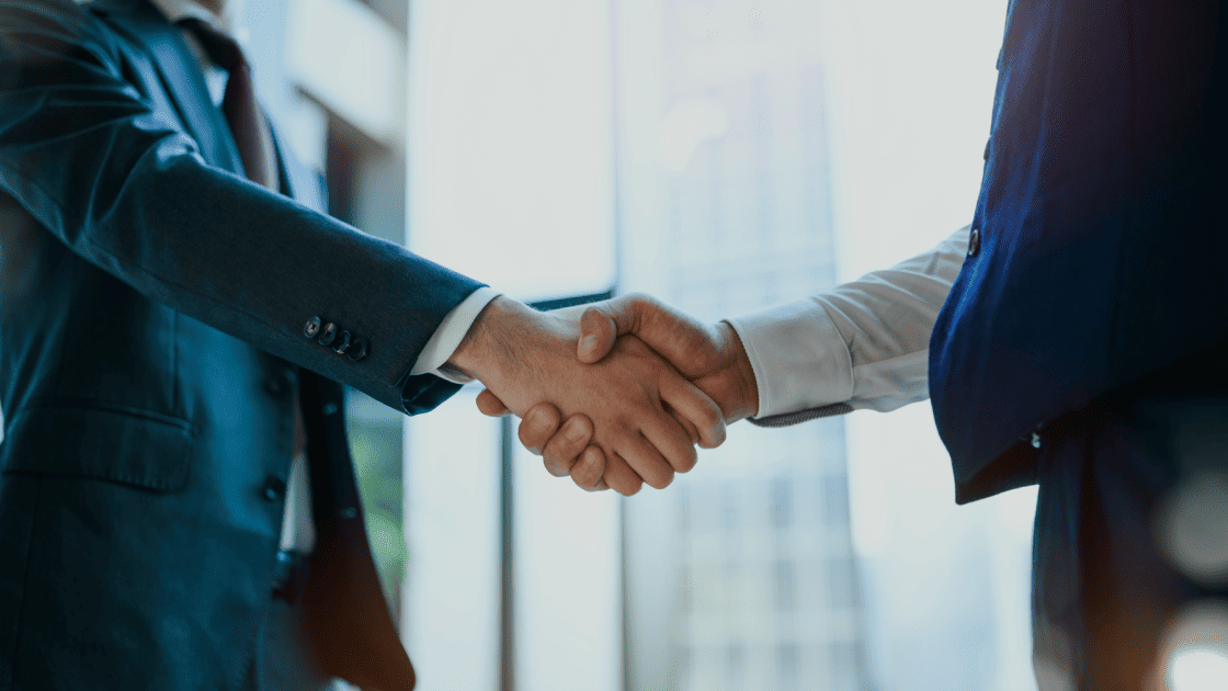 ビジネス街のオフィスで握手を交わし、売れるまで伴走するパートナーシップを象徴するシーン