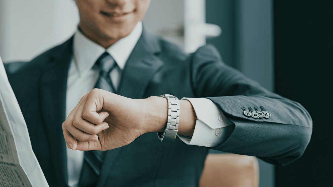 腕時計で時間を確認しながら微笑むスーツ姿のビジネスパーソンが、素早い意思決定とスピード対応をイメージさせるシーン