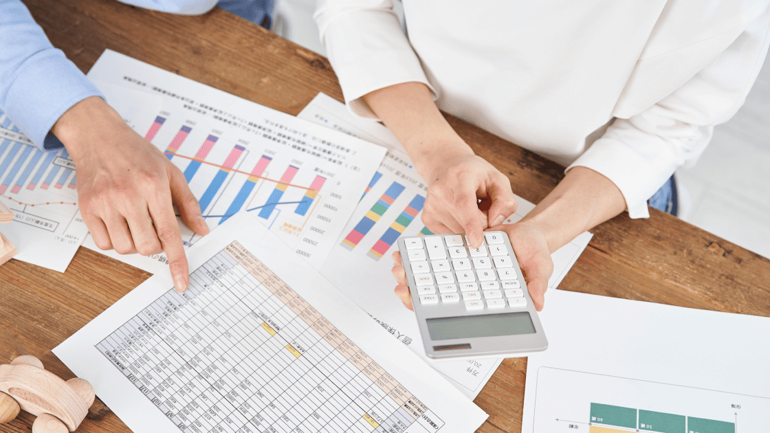 グラフや一覧表の資料を前に、電卓を操作しながら価格シミュレーションや収益計算を行う担当者の手元
